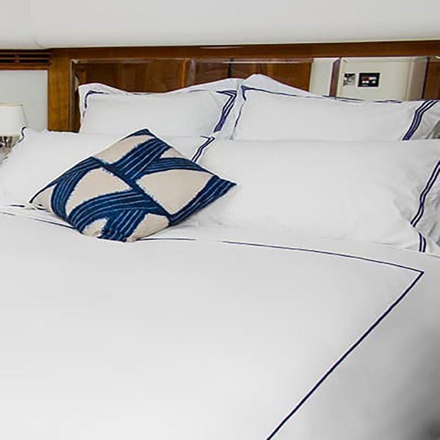 Luxury bespoke bed linen set with white cotton fabric and blue embroidery, tailored for yachts and marine cabins in the UAE