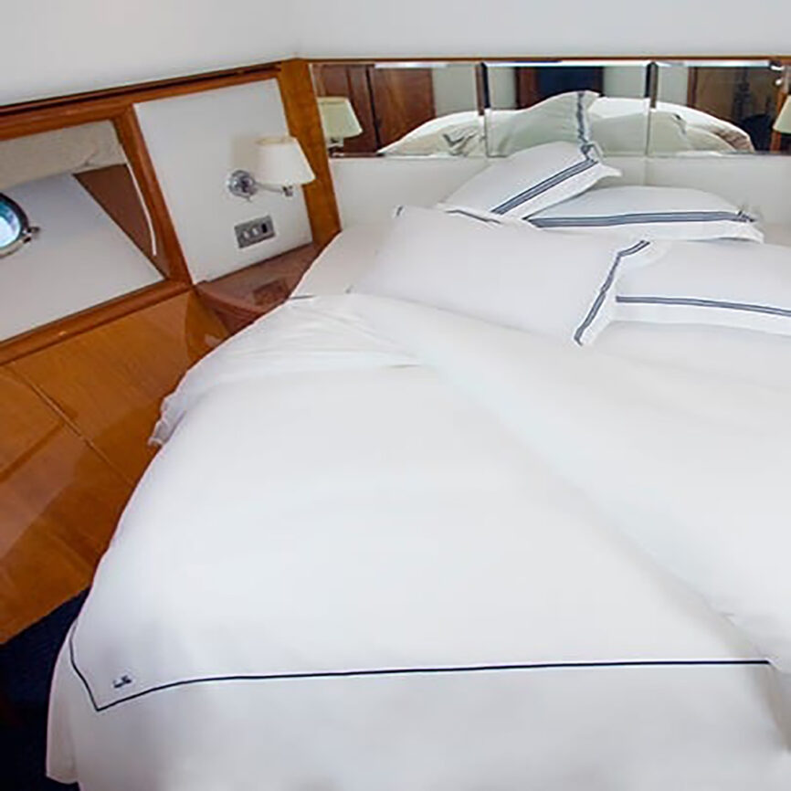 Luxury bespoke bed linen set with white cotton fabric and blue embroidery, tailored for yachts and marine cabins in the UAE