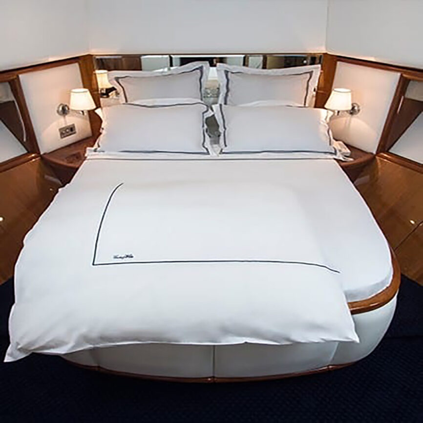 Luxury bespoke bed linen set with white cotton fabric and blue embroidery, tailored for yachts and marine cabins in the UAE