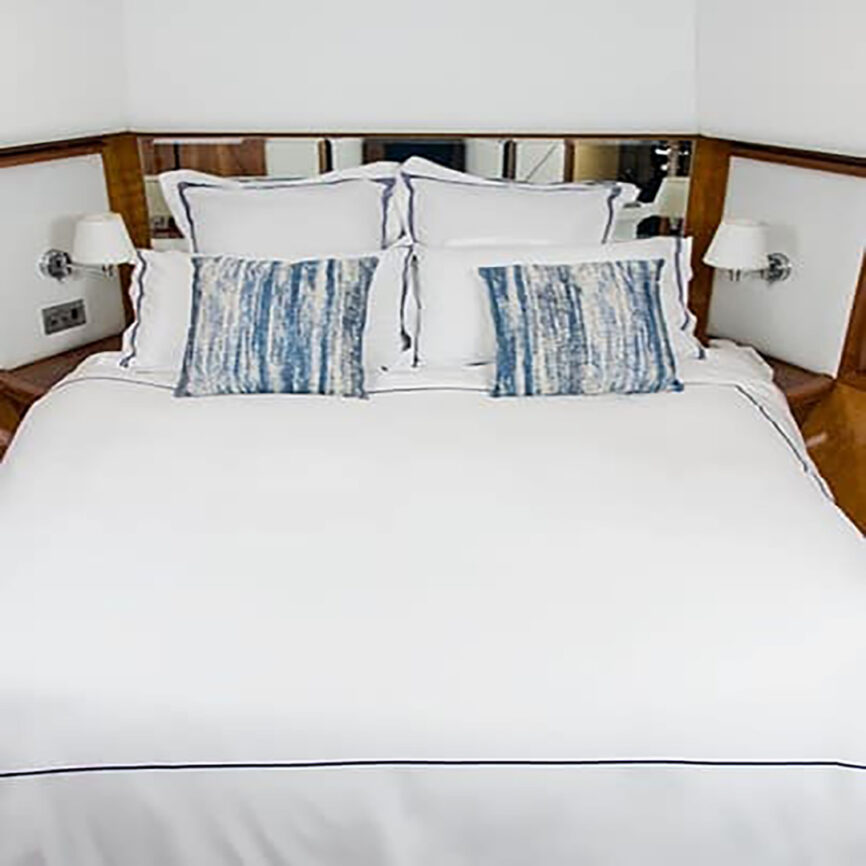 Luxury bespoke bed linen set with white cotton fabric and blue embroidery, tailored for yachts and marine cabins in the UAE